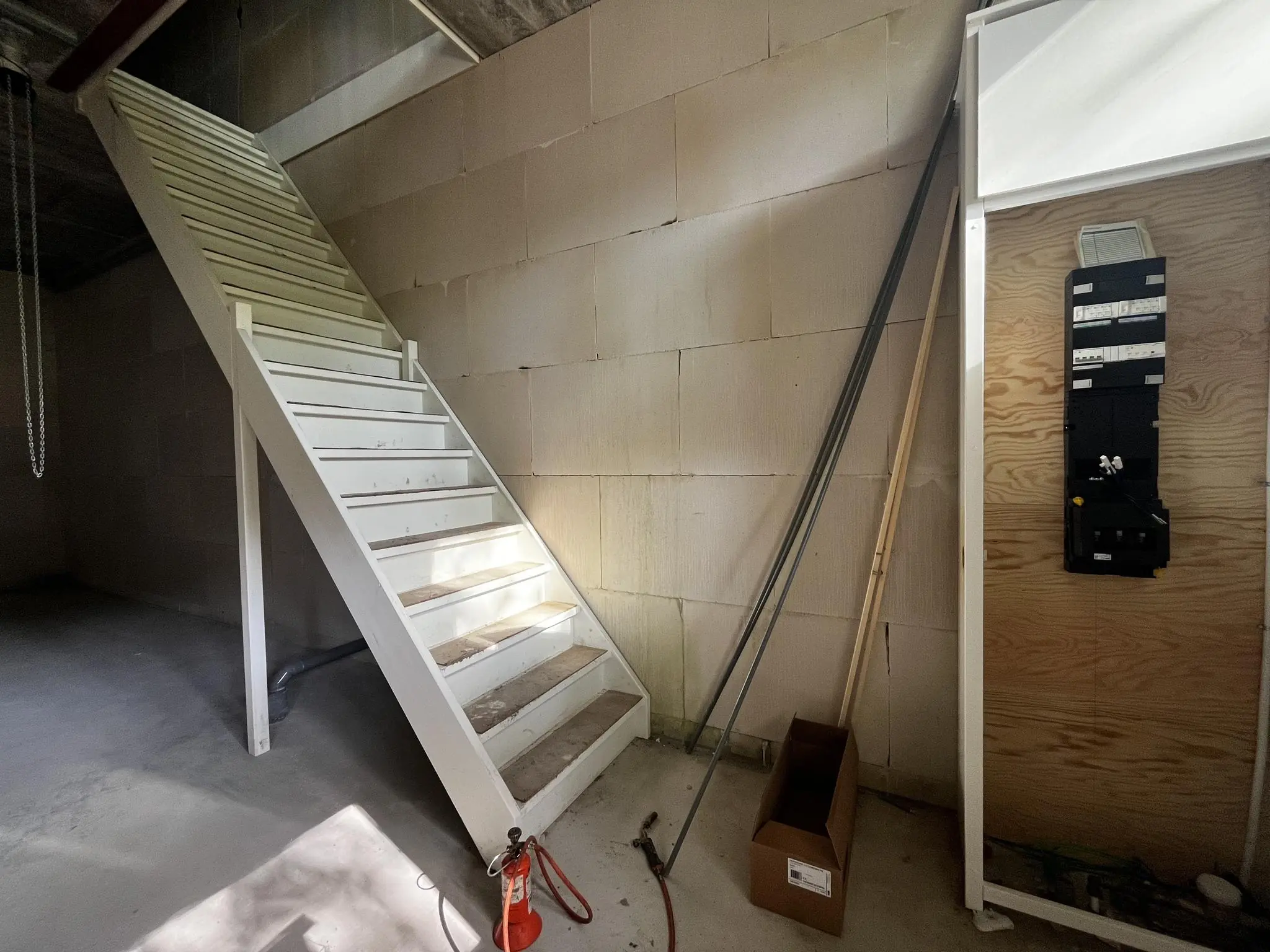 Witte houten trap in een onafgewerkte ruimte aan de Broekdijk West 19-10, met meterkast en bouwmaterialen.